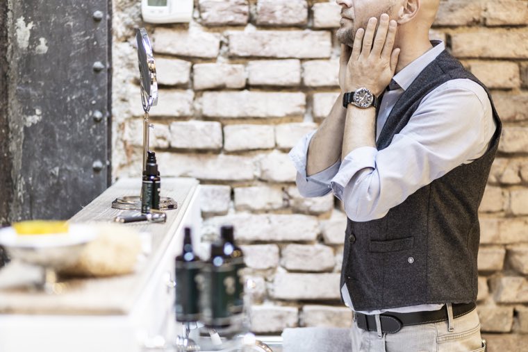 Mann vor Spiegel im Badezimmer, cremt sich ein