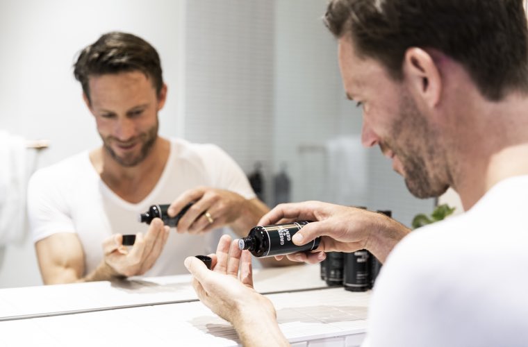 Mann vor Spiegel im Badezimmer, schüttet sich After Shave in die Hand