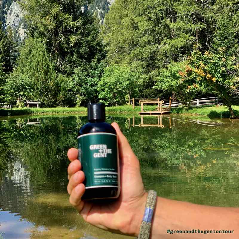 Shampoo + Body Wash von GREEN + THE GENT, gehalten in einer Hand vor einem Teich in den Bergen von Meran